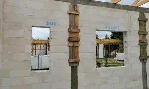 Ściana z bloczków z otworami okiennymi i drewnianymi szalunkami, w trakcie budowy.