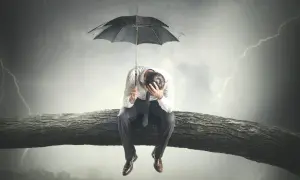 Uomo seduto su un ramo d'albero sotto un temporale, con un ombrello. Sembra che il mio ragazzo è depresso, perso nei suoi pensieri.