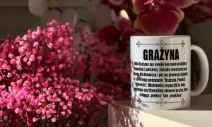 Kubek z napisem "Grażyna" na imieniny, otoczony delikatnymi, różowymi kwiatami.