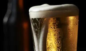 Bicchiere di birra olandese dorata con schiuma bianca e goccioline di condensa, su sfondo scuro.