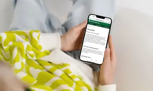 Person håller upp en mobiltelefon som visar Försäkringskassans SGI-guide. Guiden förklarar vad SGI är och hur den fungerar för enskild firma.