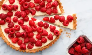 Pyszna tarta z malinami, udekorowana kremem i świeżymi malinami. Jeden kawałek już został wyjęty.