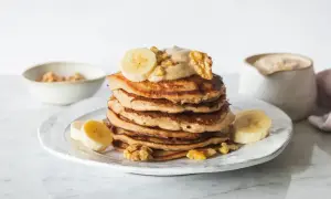 Stos placuszków bananowych z kremem, bananami i orzechami włoskimi na talerzu.