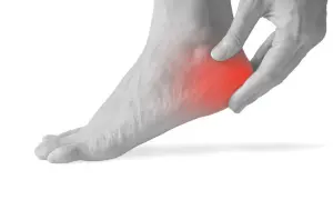 Mano che preme sul tallone sinistro, evidenziato in rosso, per indicare il dolore.