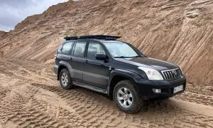 Czarny Land Cruiser 120 na piaszczystym podłożu, z bagażnikiem dachowym, gotowy na terenową przygodę.