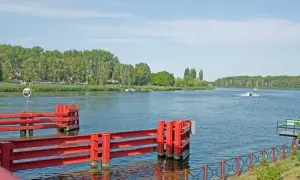 Czerwone śluzy wodne w Dziwnowie nad morzem, z zielonymi drzewami w tle i skuterem wodnym na wodzie.