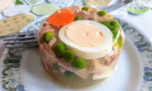 Galareta z kurczaka z jajkiem, groszkiem i marchewką na talerzu.