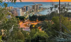 Malaga co zobaczyc: widok na port i miasto o zachodzie słońca z zielonymi drzewami na pierwszym planie.
