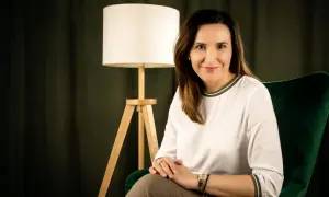 Kobieta w białej bluzce siedzi w zielonym fotelu obok lampy.