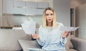 Zaskoczona kobieta z papierami w rękach, liczy rachunki. Czy to spadek po rodzicach?