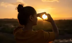 Silueta de mujer haciendo un corazón con las manos al atardecer, reflejando su actitud positiva ante la vida.