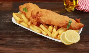 Un delicioso plato típico inglés: pescado rebozado y patatas fritas crujientes, servido con rodajas de limón y perejil.