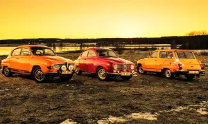 Tre klassiska Saab-bilar, en röd och två orange, står uppradade i solnedgången. En laban bil som väcker nostalgi.
