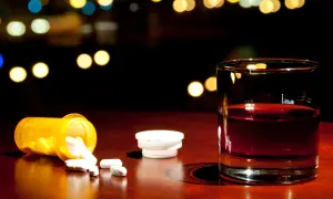 Szklanka z alkoholem i rozsypane tabletki paracetamolu na drewnianym blacie.