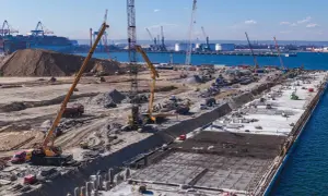 Budowa dużego portu w Japonii. Dźwigi, koparki i ciężarówki pracują na placu budowy, tworząc nową infrastrukturę.