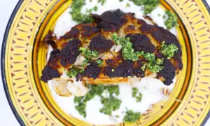 Un chou-fleur rôti, bien caramélisé, servi sur une sauce blanche crémeuse et garni d'une sauce verte et de graines.