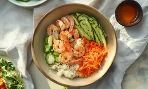 Kolorowy poke bowl z krewetkami, ryżem, ogórkiem i startą marchewką, posypany czarnym sezamem. Idealny na lekki posiłek.