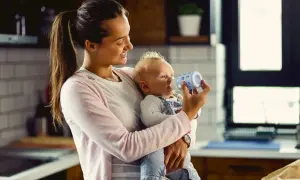 Uśmiechnięta mama karmi butelką niemowlę. Kiedy można podać koperek dla noworodka? To pytanie nurtuje wielu rodziców.