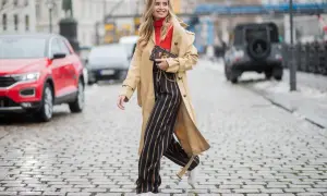 Frau in Beige-Trenchcoat, rotem Rollkragenpullover und gestreiften Hosen, die zeigt, wie man einen Trenchcoat kombinieren kann.