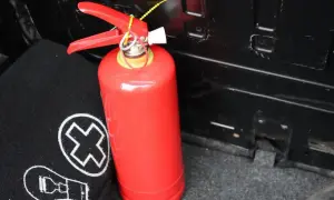 Czerwona gaśnica, kluczowa w definicji bezpieczeństwa, stoi obok czarnego materiału z białymi symbolami.