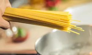 Dłoń trzymająca pęczek spaghetti nad gotującą się wodą. Zastanawiasz się, jaki makaron ma najmniej kalorii?