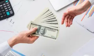Przekazanie pieniędzy na rachunek bankowy. Dłonie przekazują stos banknotów 100 dolarowych.