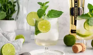 Orzeźwiający Hugo Spritz z limonką i miętą, idealny na letnie popołudnie. Obok butelka St-Germain.