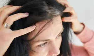 Mani che toccano capelli scuri con ciocche bianche, un segno di come cambiano i capelli nel tempo.