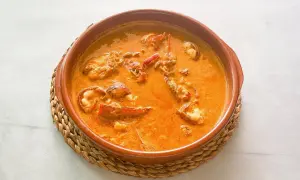 Caldereta de langosta, un plato de marisco reconfortante en una cazuela de barro, con trozos de langosta en una salsa naranja cremosa.