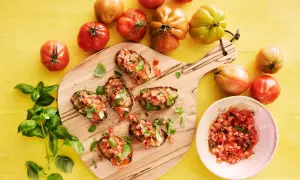 Bruschetta recept med färska tomater och basilika på en träskärbräda, omgivet av mogna tomater.