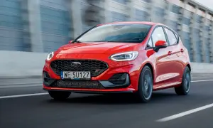 Czerwony Ford Fiesta ST pędzi po drodze, błyszcząc w słońcu.