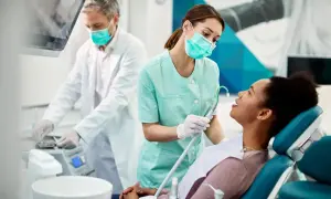 Uśmiechnięta asystentka stomatologiczna w maseczce i rękawiczkach przygotowuje pacjentkę do zabiegu.