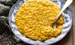Un cremoso risotto alla zucca, servito su un piatto decorato, con una forchetta che affonda nel piatto.