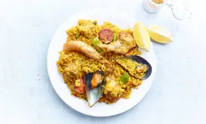 Une assiette de paella royale, garnie de crevettes, moules, poulet, chorizo et riz jaune, avec des quartiers de citron.