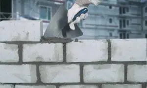 Maurer legt Mörtel mit Kelle auf Ziegelsteine. Der Unterschied zwischen Zement und Beton wird hier beim Mauern deutlich.