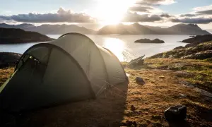 Zielony namiot na skalistym wybrzeżu, z widokiem na morze i góry. Czy można rozbić namiot na dziko na wyspach u wybrzeży Norwegii? Tak, to idealne miejsce.