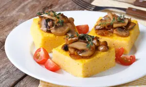 Trzy kwadratowe porcje polenty, podane z duszonymi pieczarkami i pomidorkami koktajlowymi. Pyszne danie, które pokazuje, co to polenta.