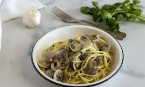 Un piatto invitante di spaghetti con le vongole, conditi con prezzemolo fresco e serviti in una ciotola bianca.