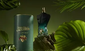 Flakon perfum Jean Paul Gaultier Le Beau Le Parfum w otoczeniu zielonych liści i mchu.