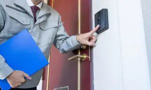 Mężczyzna w szarym stroju roboczym z teczką naciska domofon. Może to być kontrola z ZUS na L4.