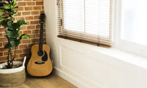 Akustyczna gitara, idealna na sto lat na gitarze dla początkujących, stoi przy ceglanej ścianie obok rośliny w koszu.