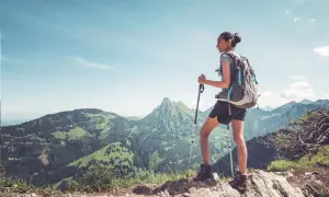 Dziewczyna z plecakiem i kijkami trekkingowymi podziwia górski krajobraz. Pokazuje, jak chodzić z kijkami trekkingowymi, by czerpać radość z wędrówki.