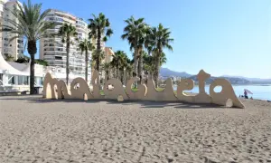 Malaga plaże: piasek, palmy i napis "Malaga" na tle budynków i morza.