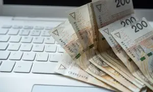 Banknoty 200 zł leżące na białej klawiaturze laptopa.