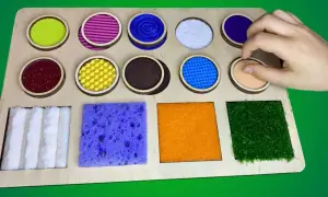 Tabla sensorial con diversos tipos de texturas para niños: círculos con materiales variados y cuadrados con esponja, fieltro y césped artificial.
