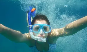 Dziewczyna w masce i rurce do oddychania pływa pod wodą. To właśnie snorkeling – odkrywanie podwodnego świata!