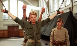 David Bowie jako major Celliers, pojmany w "Merry Christmas Mr. Lawrence", z rękami przykutymi do łańcuchów. Obok stoi japoński oficer.