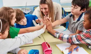 Niños y maestra celebran con un choque de manos, fomentando la motivación en el aula.