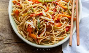Un piatto invitante di spaghetti di riso saltati con verdure colorate e semi di sesamo, pronti per essere gustati con le bacchette.