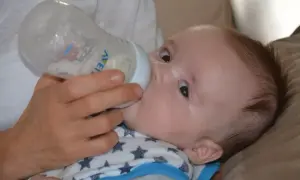 Rączka podaje butelkę z mlekiem 5-miesięcznemu dziecku, które pije z zapałem.